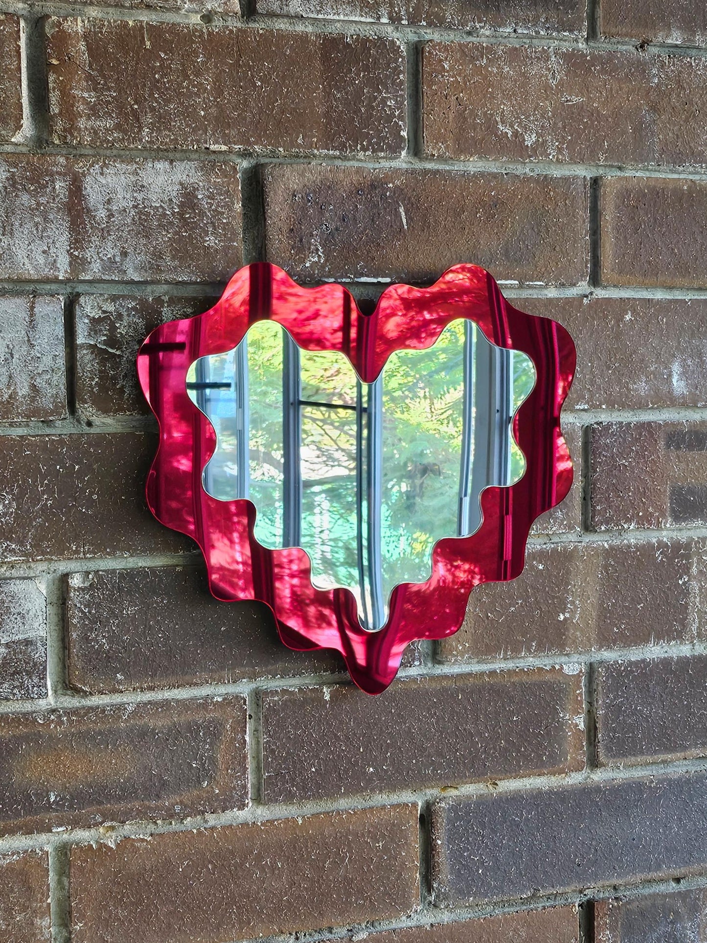 Decorative red mirror with a wavy edge on a brick wall