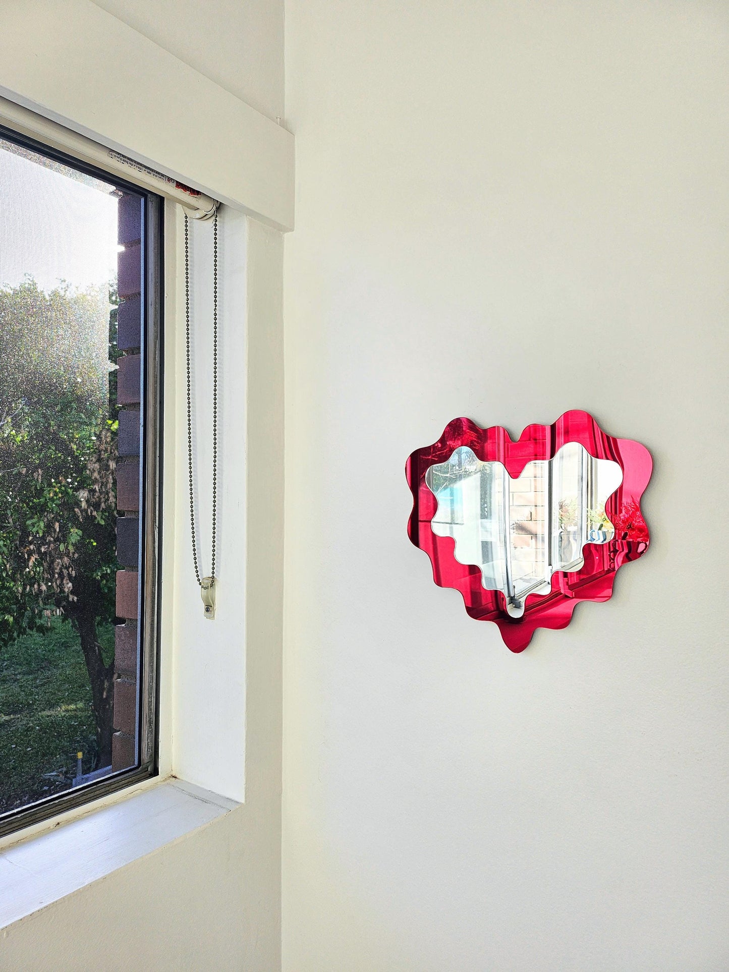 Heart-shaped decorative item on a wall next to a window with a view of trees.