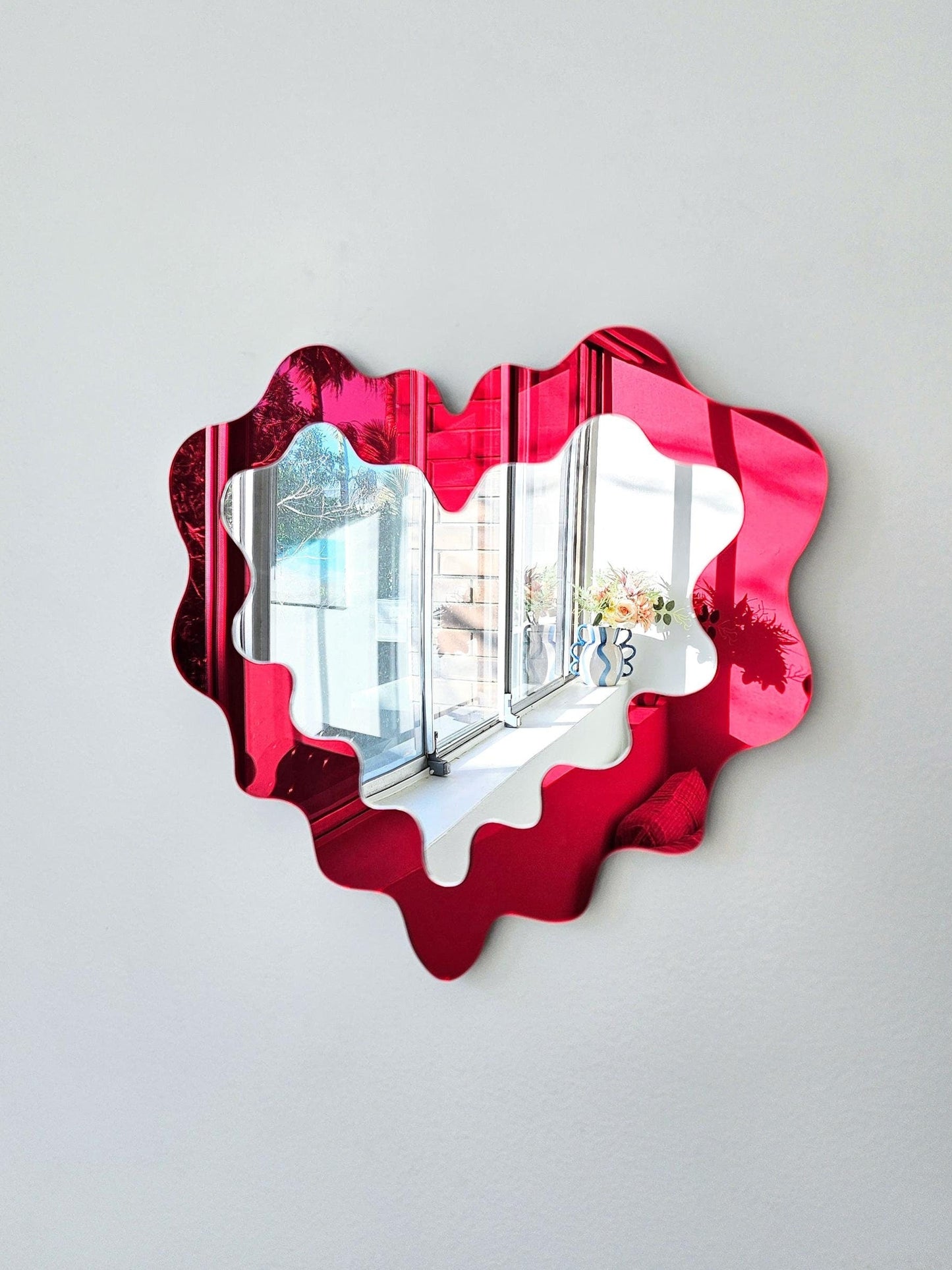 Heart-shaped mirror with red frame on a white wall